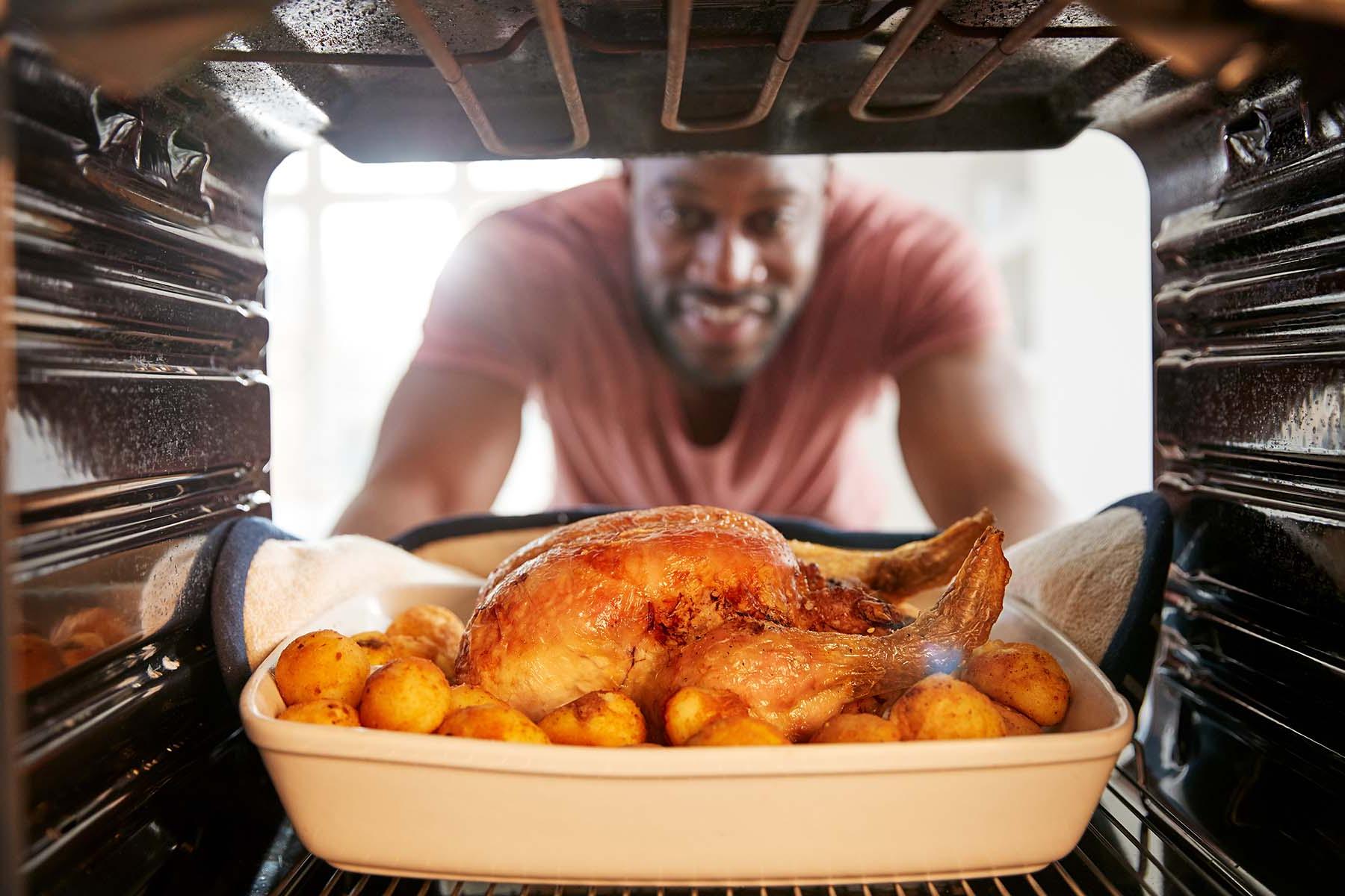 A man smiles as he takes a roasted chicken out of the oven